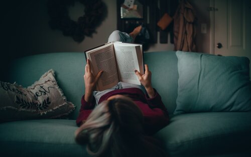 A woman reading a book on a green couch in her library | © Unsplash.com