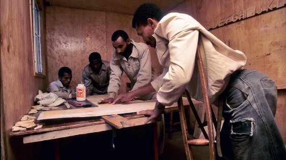 There are 4 men, working on wood and other material in an informal workspace