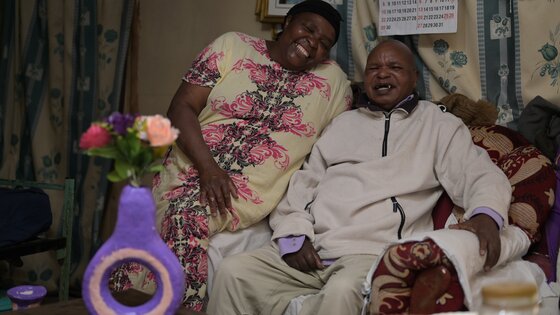 Elderly man and woman sitting on the couch next to each other laughing 